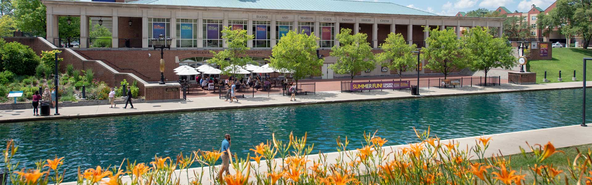 Exterior of History Center taken from across Canal with flowers in foreground. People are eating on the terrace.